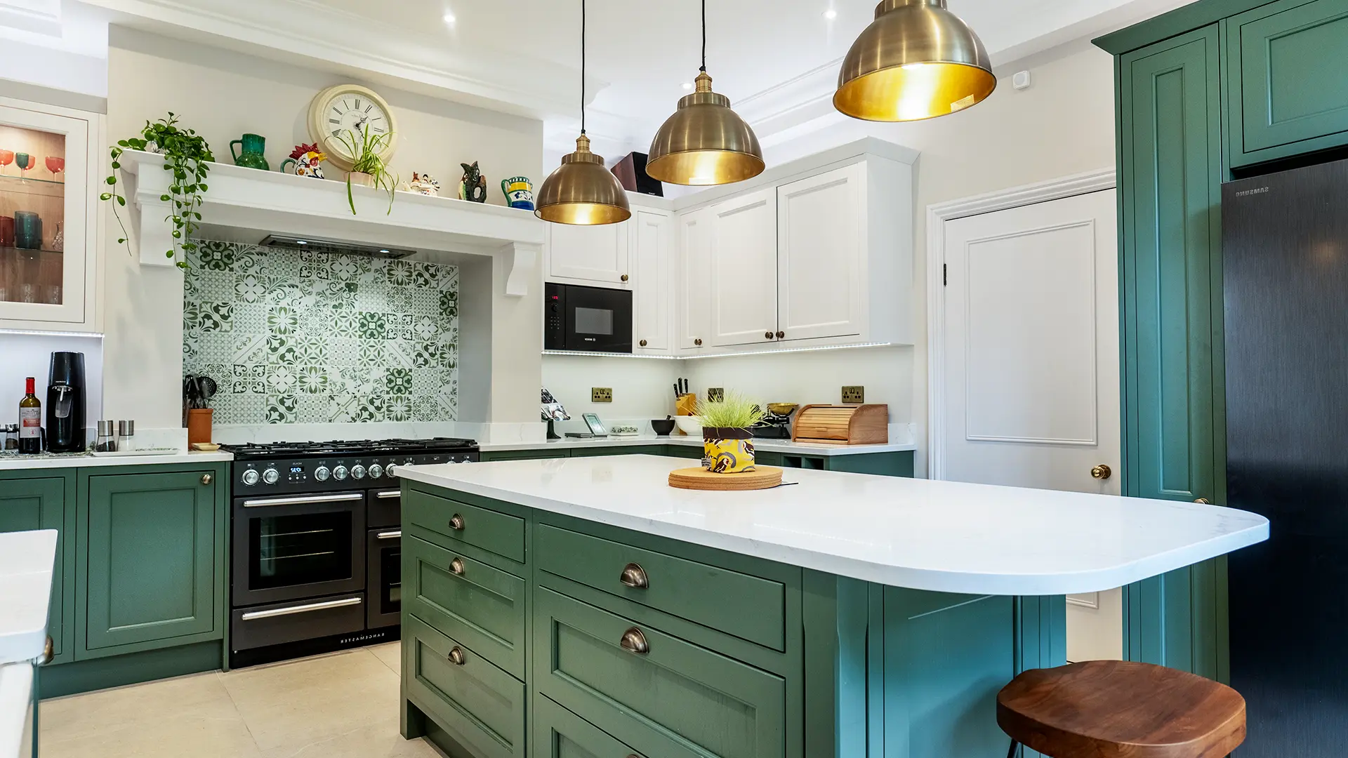 Bespoke kitchen design featuring deep green shaker cabinets, patterned splashback tiles, and brass pendant lights over a white island.