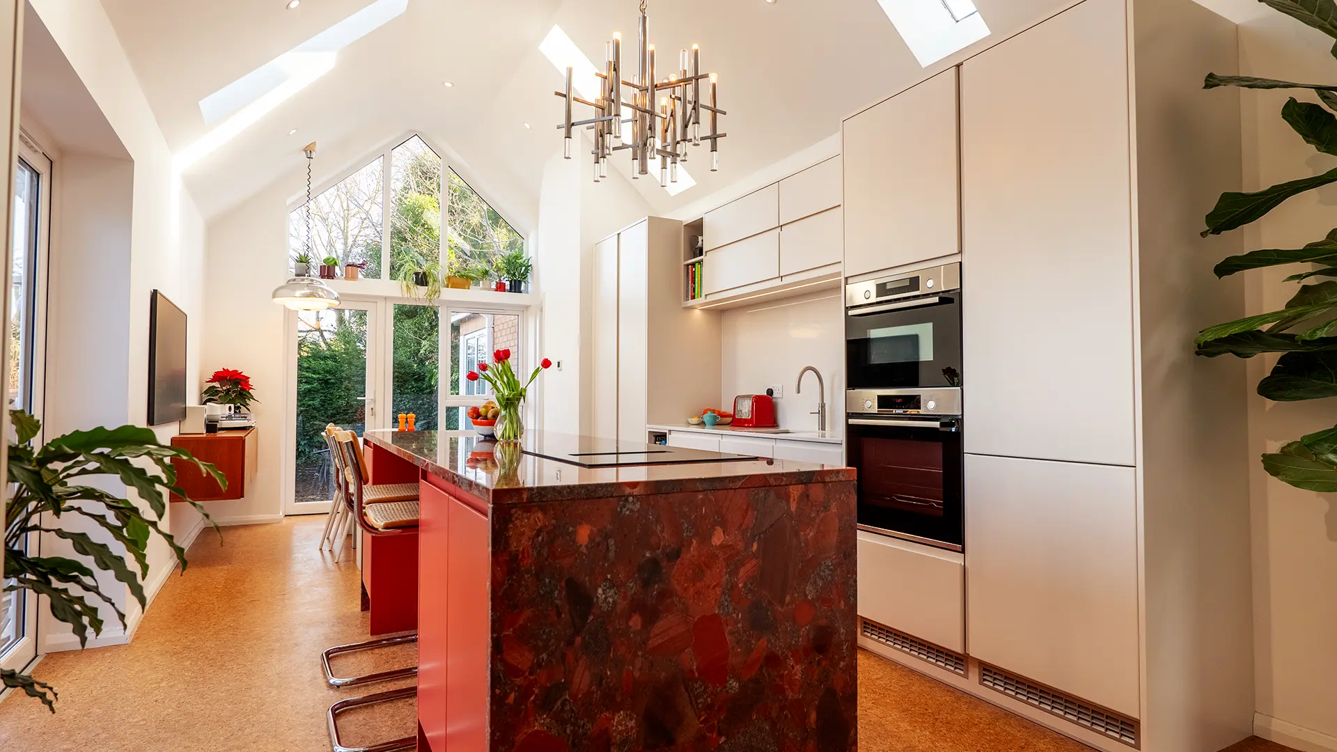 Luxury contemporary kitchen with a dramatic red stone island, minimalist white cabinetry, and vaulted ceiling with feature lighting.