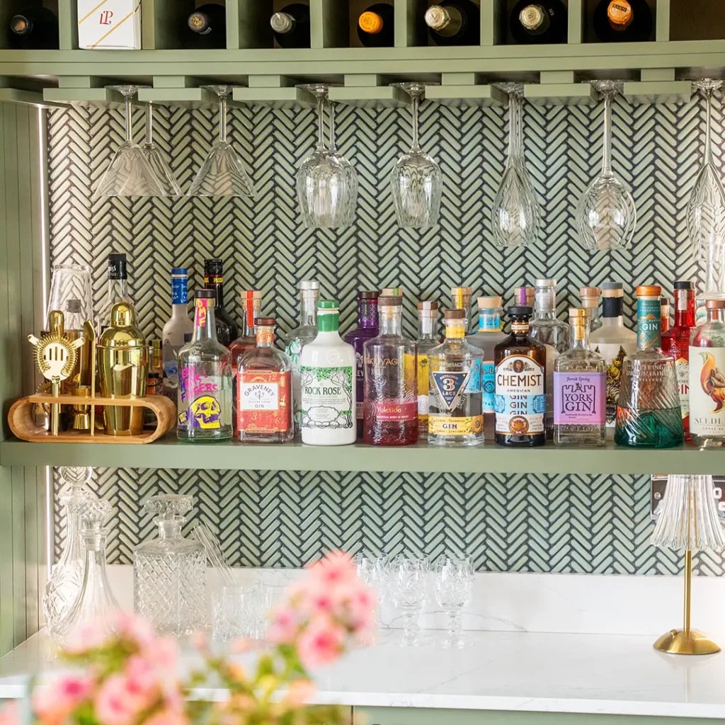 Bespoke home bar in Sheffield with green cabinetry, glassware display, and premium gin collection, designed by Designer Kitchen Direct.