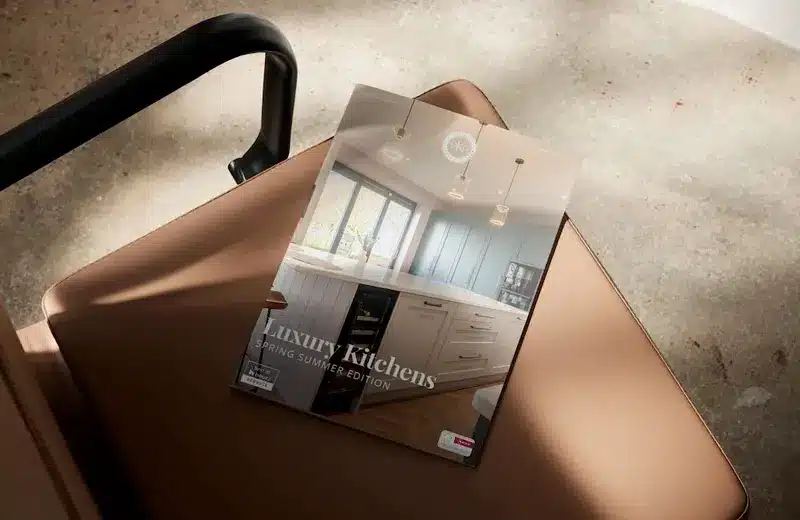 Designer Kitchen Direct luxury kitchen brochure resting on a tan leather chair in natural light.