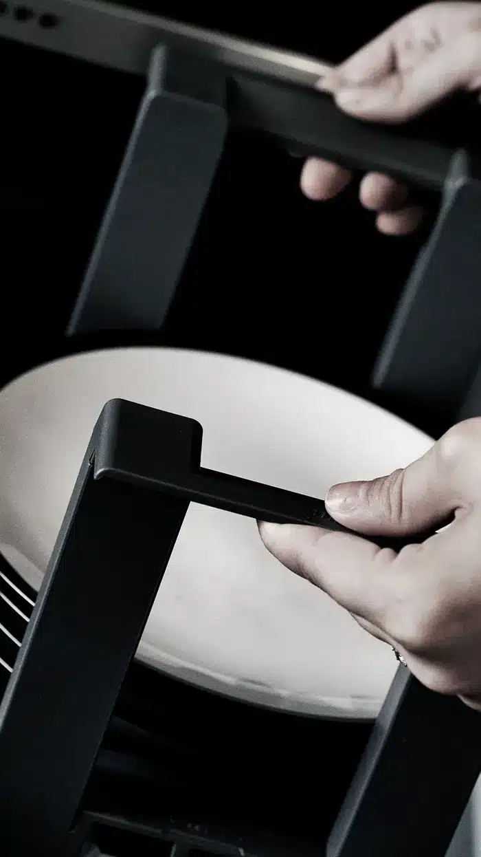 Soft-focus close-up of a plate holder being lifted inside a deep kitchen drawer, highlighting practical storage design.