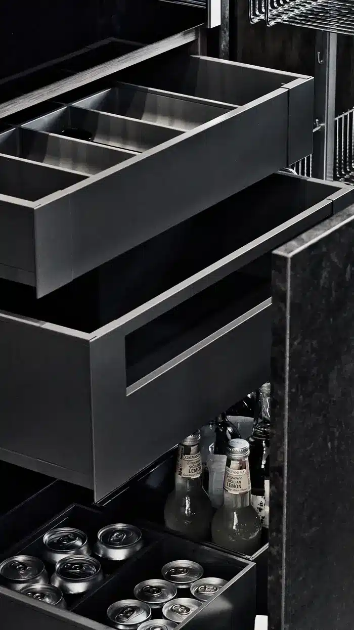 Open deep pantry drawers with sleek dividers, storing canned drinks and bottled mixers in an organised modern layout.