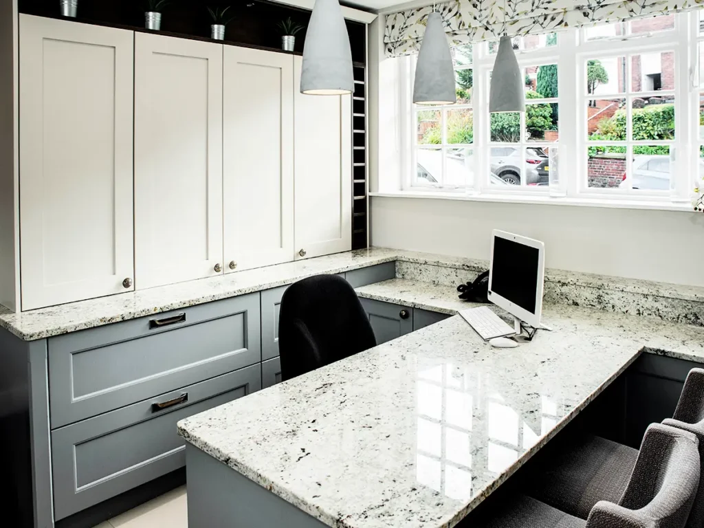 Custom luxury home office setup featuring a spacious granite desk, bespoke two-tone grey and white cabinetry, and stylish pendant lighting.