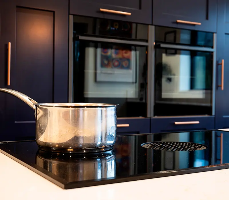 Induction hob with saucepan in a bespoke kitchen with integrated ovens