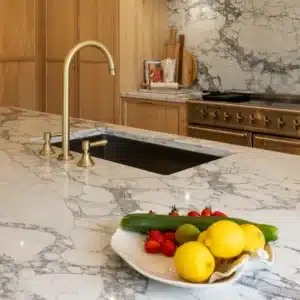 Brass kitchen tap and undermount sink set into a heavily veined stone island worktop