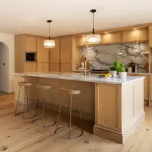 Angled view of bespoke oak kitchen island with veined stone worktop and pendant lights