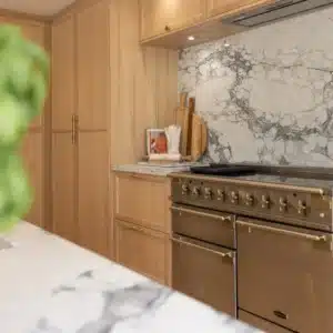 Range cooker with brass detailing beneath a dramatic full-height veined stone splashback