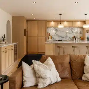 Open-plan oak kitchen viewed from the living area with island and hidden utility cabinetry